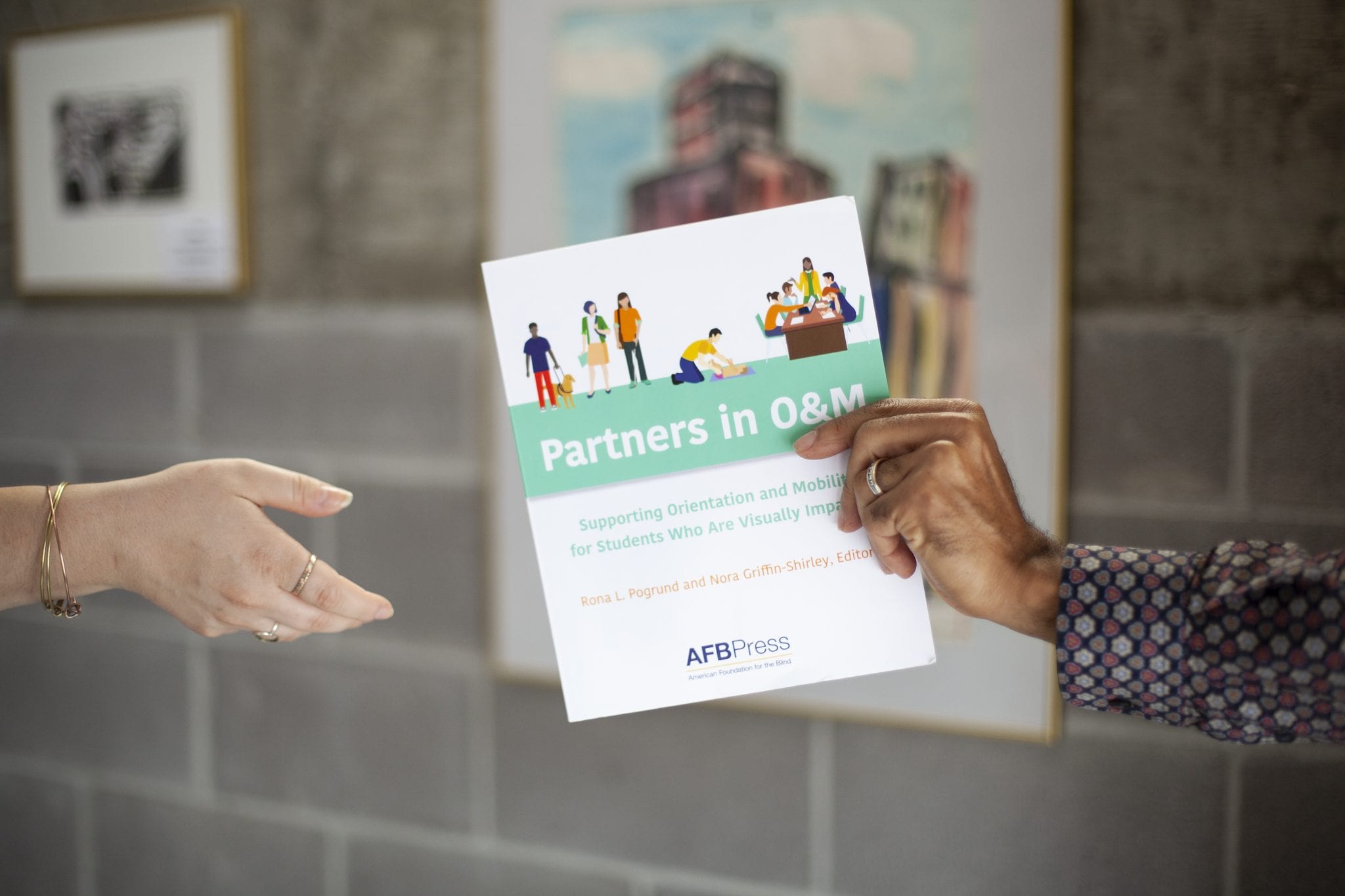 Two hands exchanging a card promoting AFB Press' Partners in O&M book