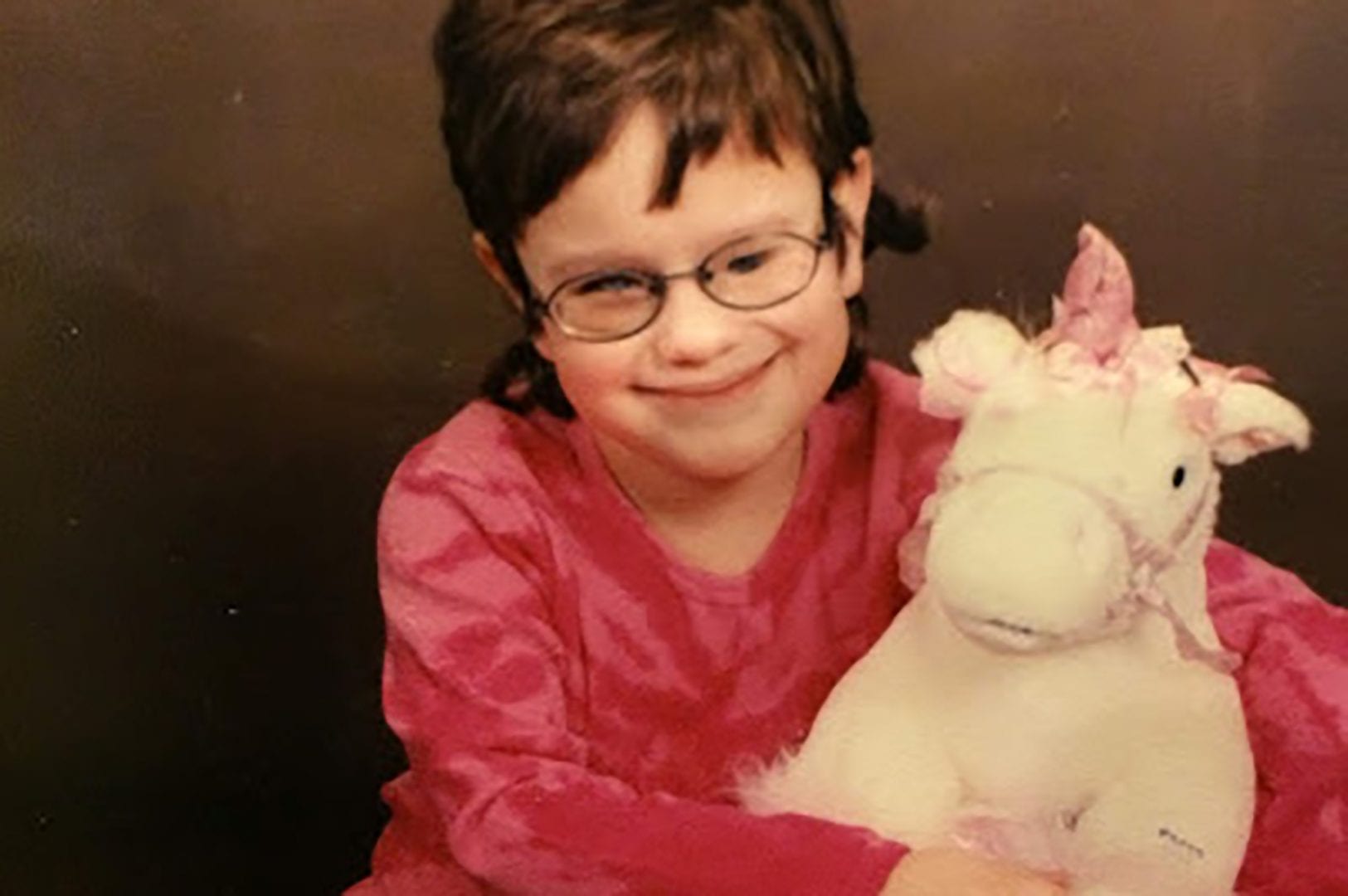 Young Jessica posing for a photo with a stuffed unicorn