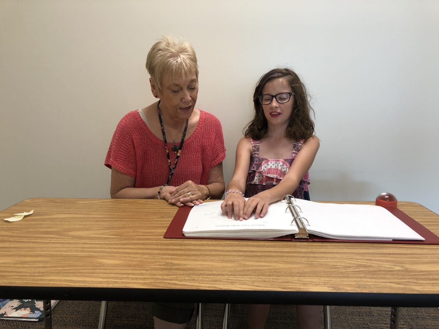 a teacher sits with a student reading at a table