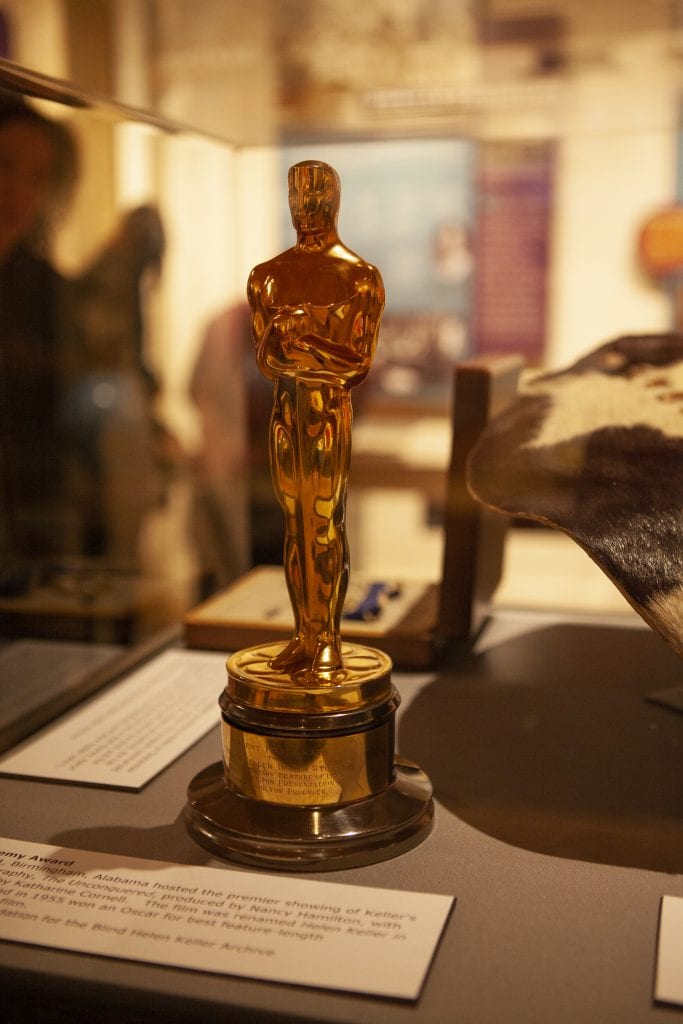 Helen Keller's academy award in a case in a museum. people out of focus in the distance