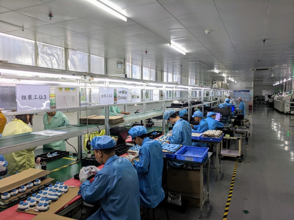 a line of factory workers in blue jackets and hats at stations producing different portions of the Code Jumper kit