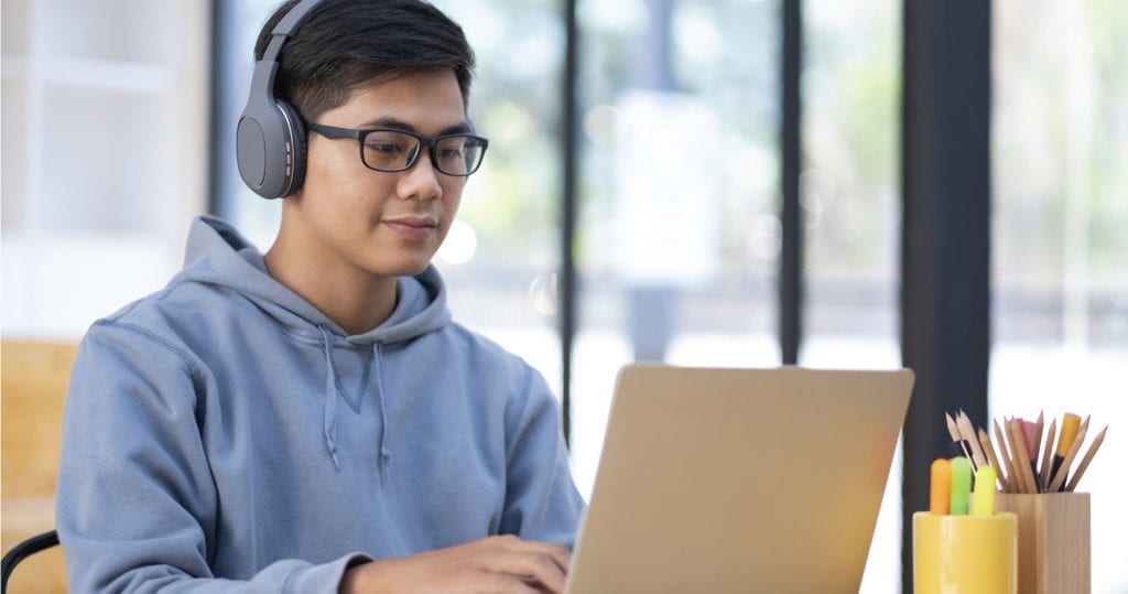 Student typing on laptop wearing headphones