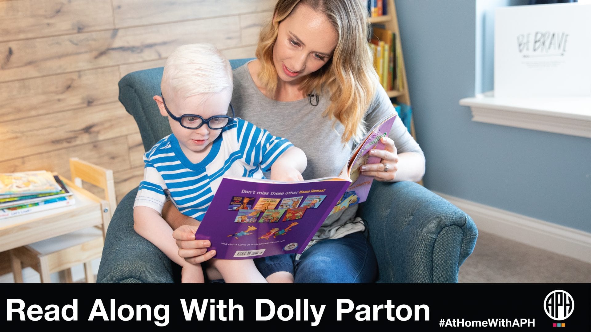 a mother and young son in glasses sitting in an arm chair reading a book. text reads "read along with Dolly Parton #AtHomeWithAPH"