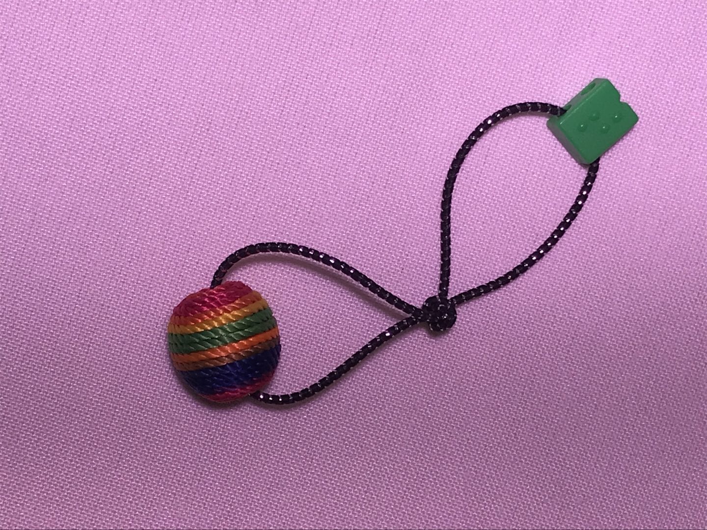 a hair elastic on a purple background. on one end is a large craft bead, on the other end is a smaller green braille bead, and in the middle the elastic is in a knot 