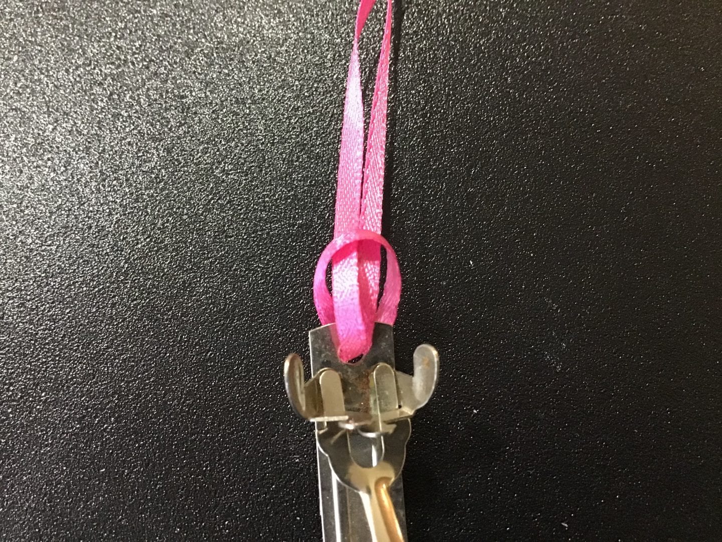 the two ends of the pink ribbon inserted through the open hole in the barrette and pulled through the loop at the other end of the ribbon