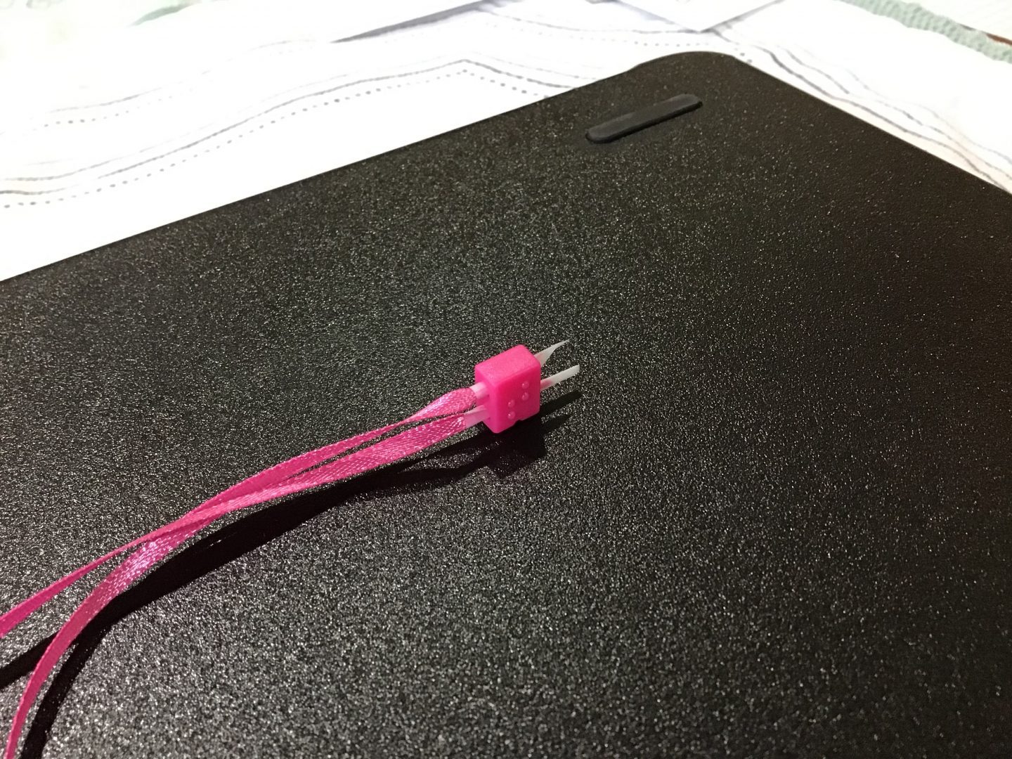 the two ends of th pink ribbon tightly wrapped in tape to make the ends rigid being inserted through the holes in a braille bead