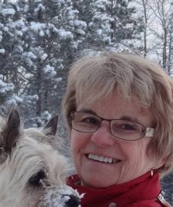 portrait photo of a woman in glasses standing outside in the snow holding a small blond dog