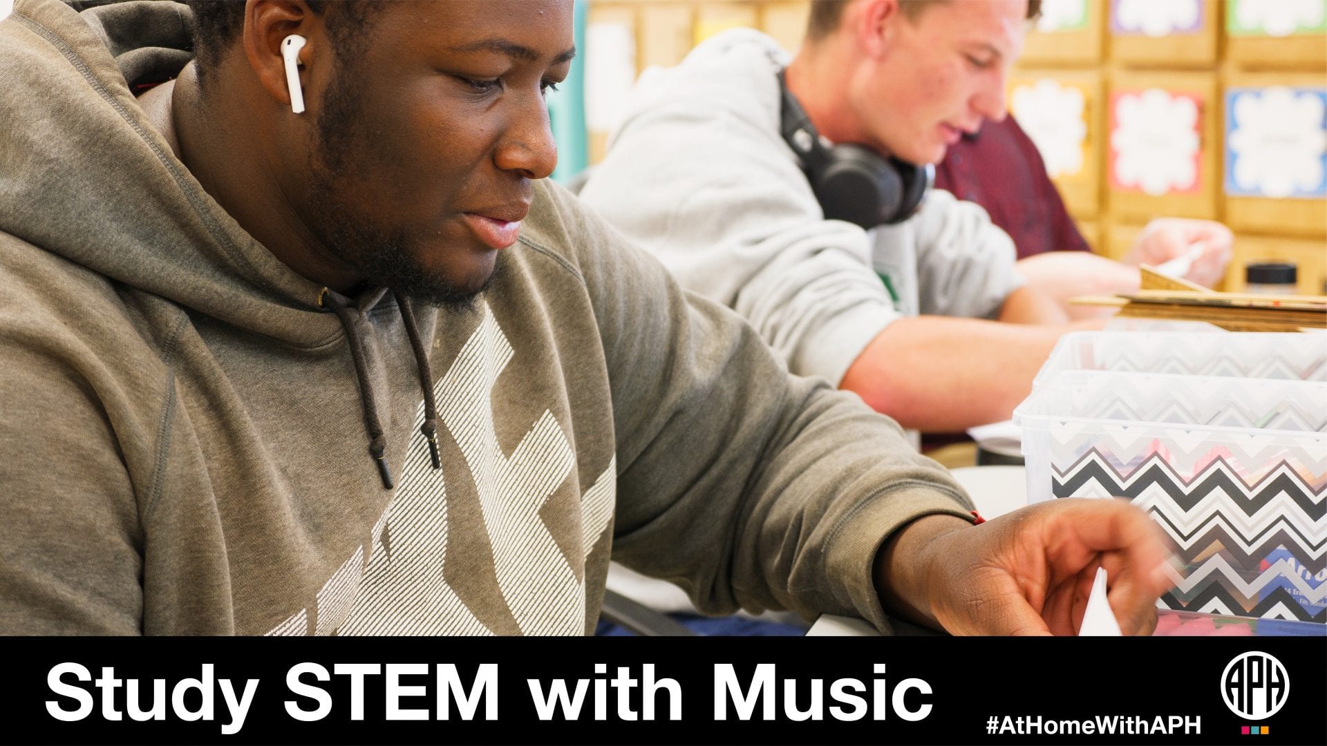 two teenage students in the classroom doing work with headphones. text reads "Studying STEM with Music #AtHomeWithAPH"