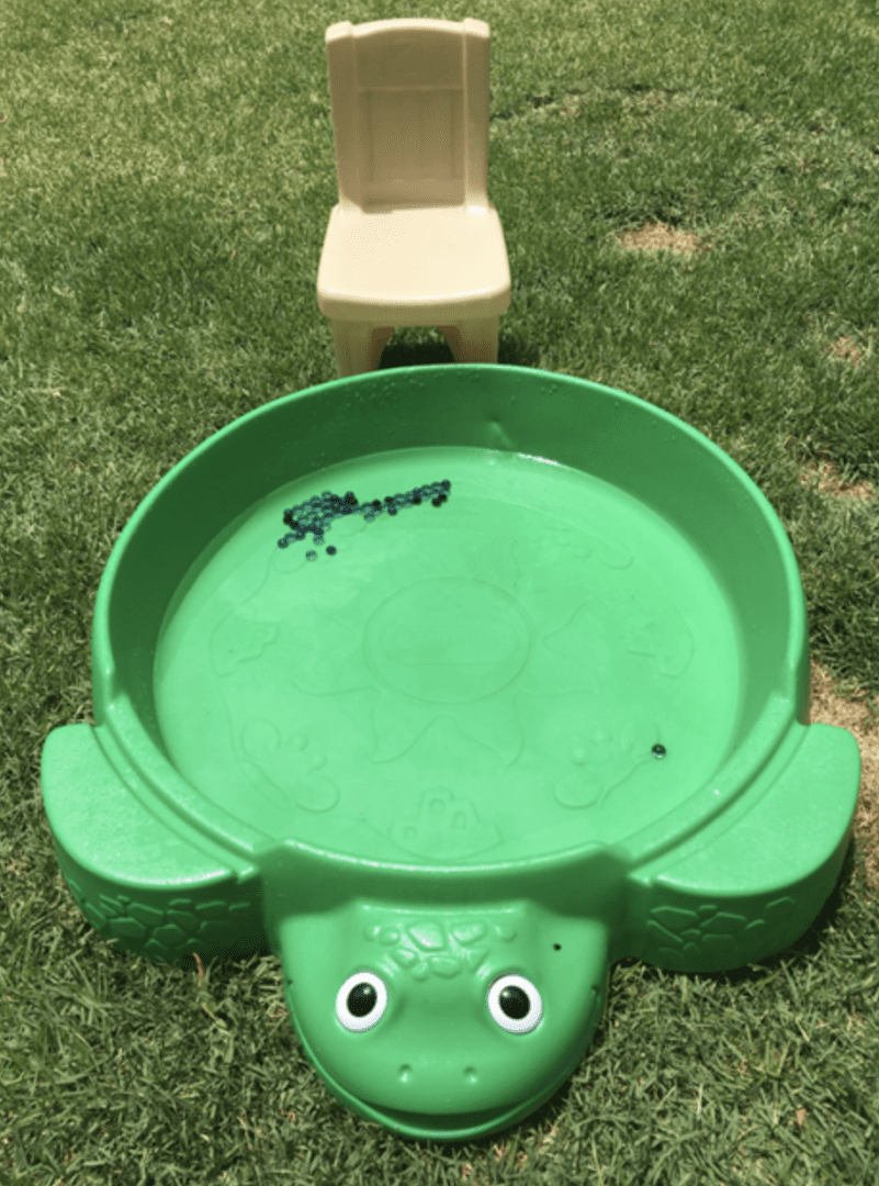 a green kiddie pool with marbles in it and a chair to the side