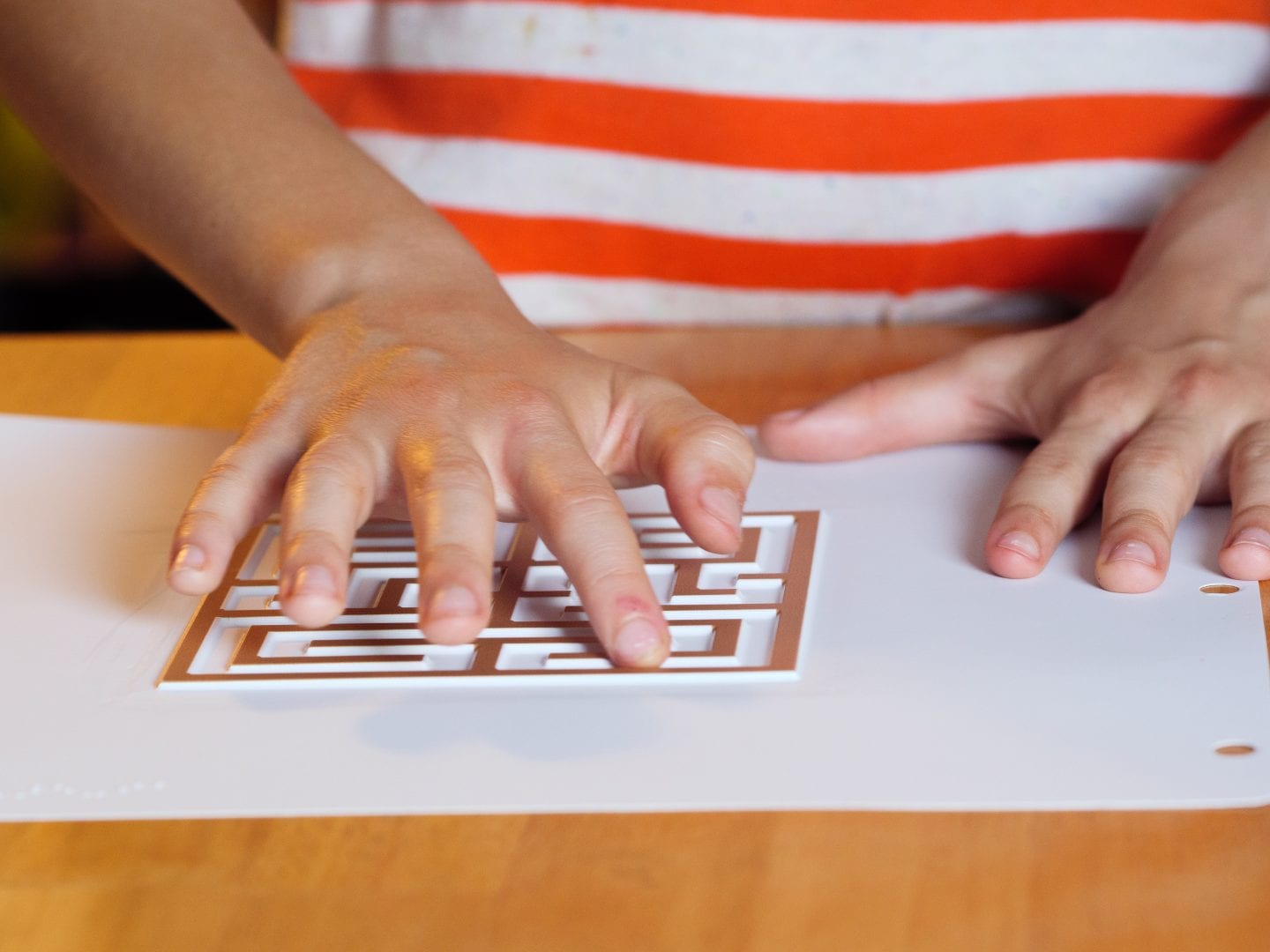 a child standing at a table with their one of their hands exploring a Finger Walks tactile labyrinth