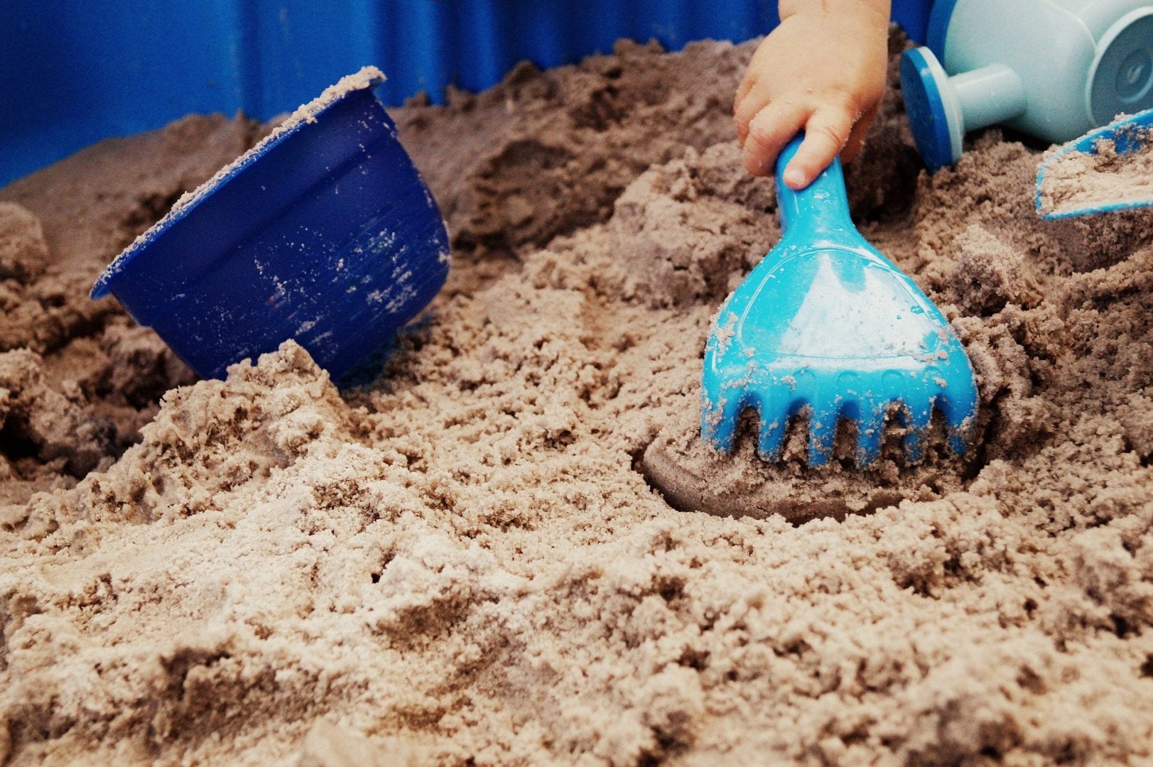 a kids hand playing with a rake and bucket in sand