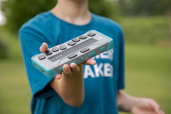 a student outside holding a chameleon 20 braille display in a teal case