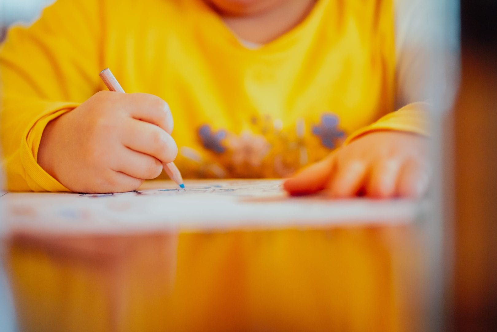 a kid in a yellow shirt coloring with a blue colored pencil