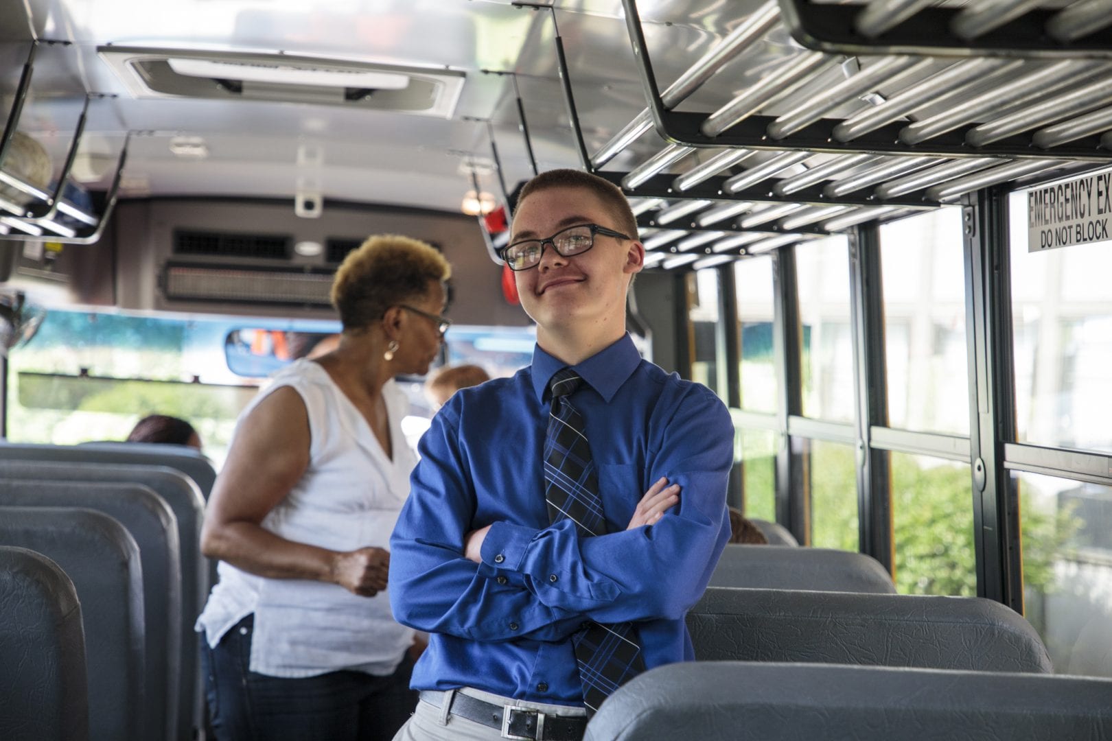 a boy on a school bus in a button up shirt and tie. His arms are crossed confidently.