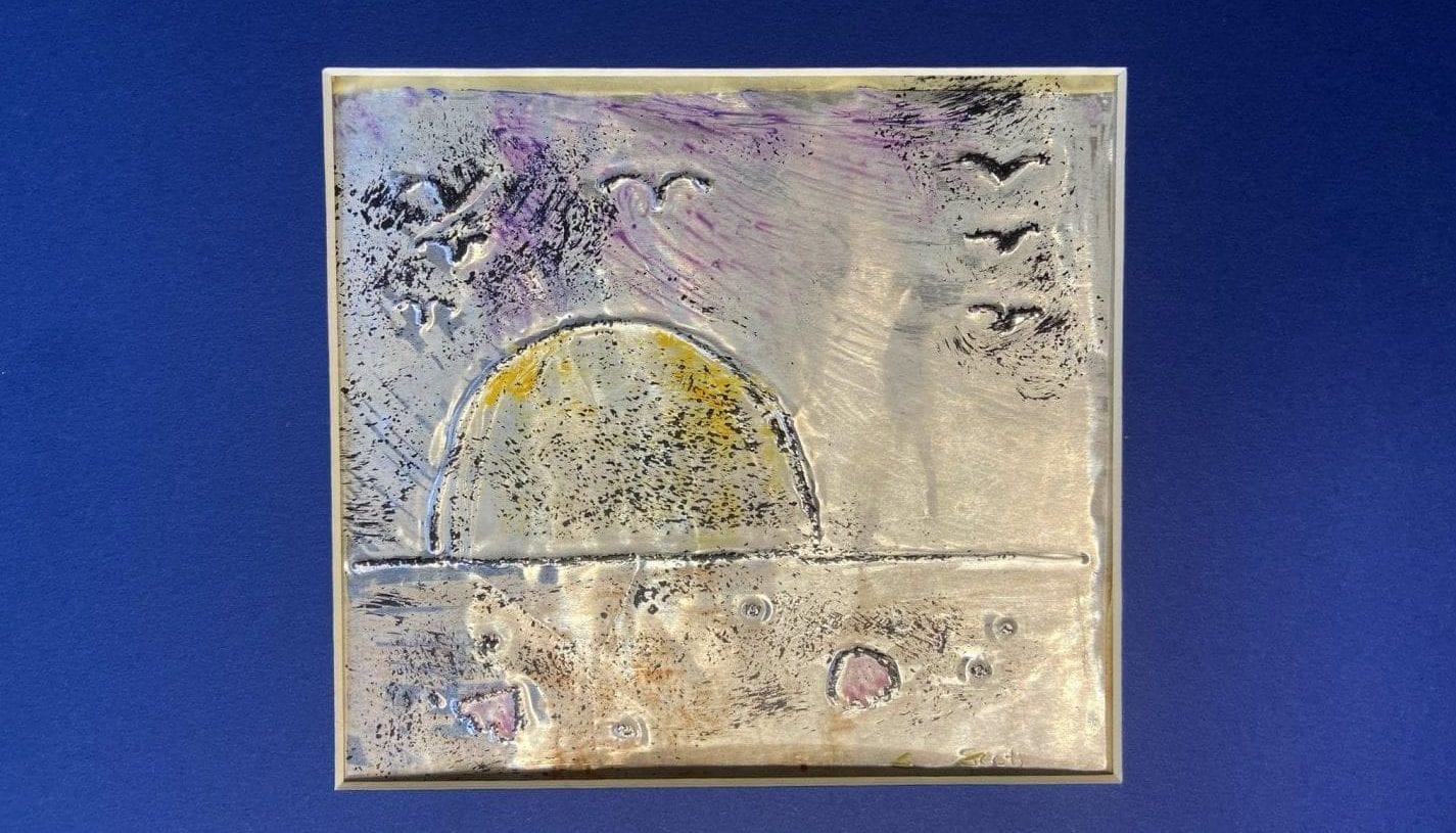 a square foil canvas on a blue background. The canvas is decorated with paint and a drawing in relief depicting a sunset on the water as seen from the beach with birds flying overhead