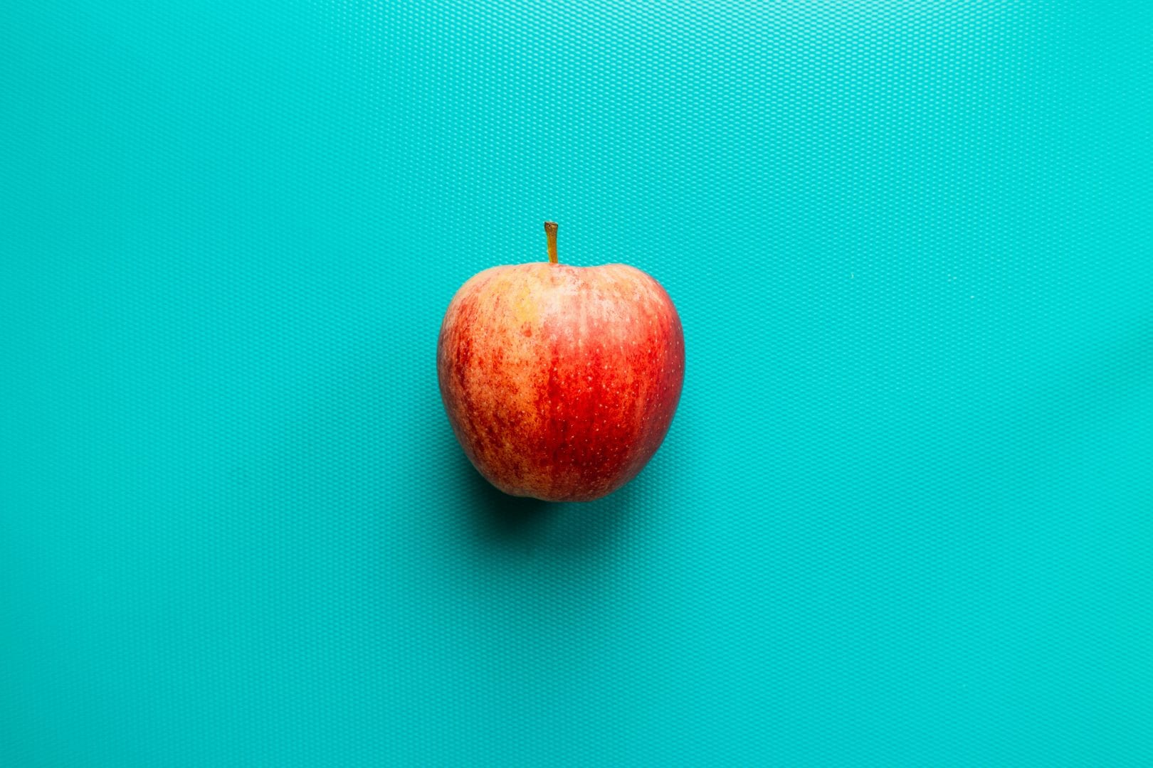 a red apple laying on a bright teal background