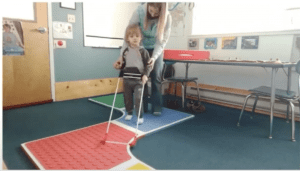 An O&M specialist worked with a preschool student to use his belt cane to walk on the path created by the Reach & Match mats.