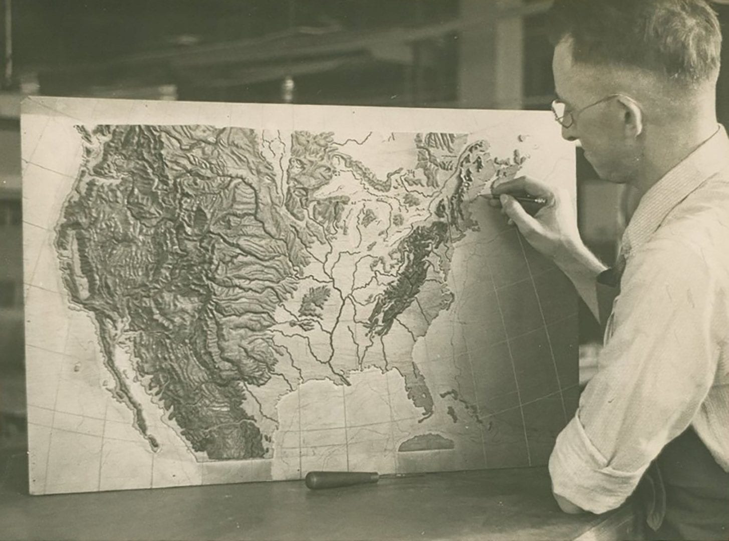 A black and white photo of a man working on the model for the US Puzzle Map