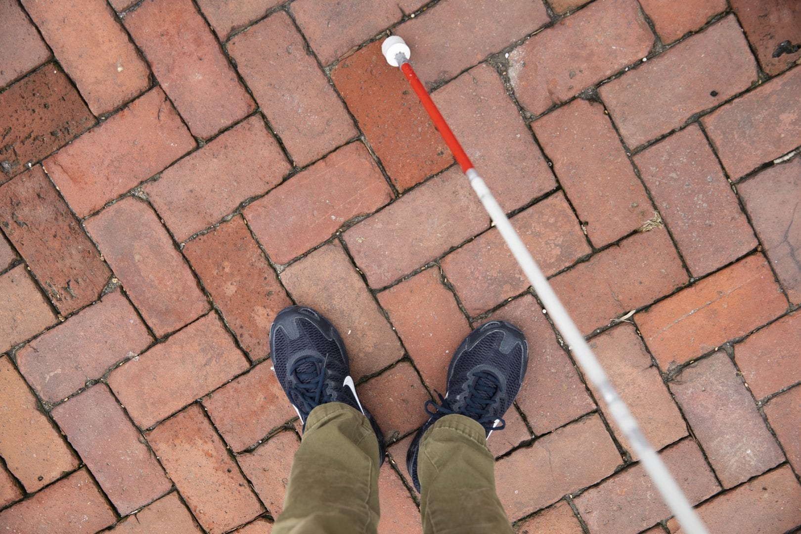 First person view looking down at feet and cane while standing on a brick walkway.