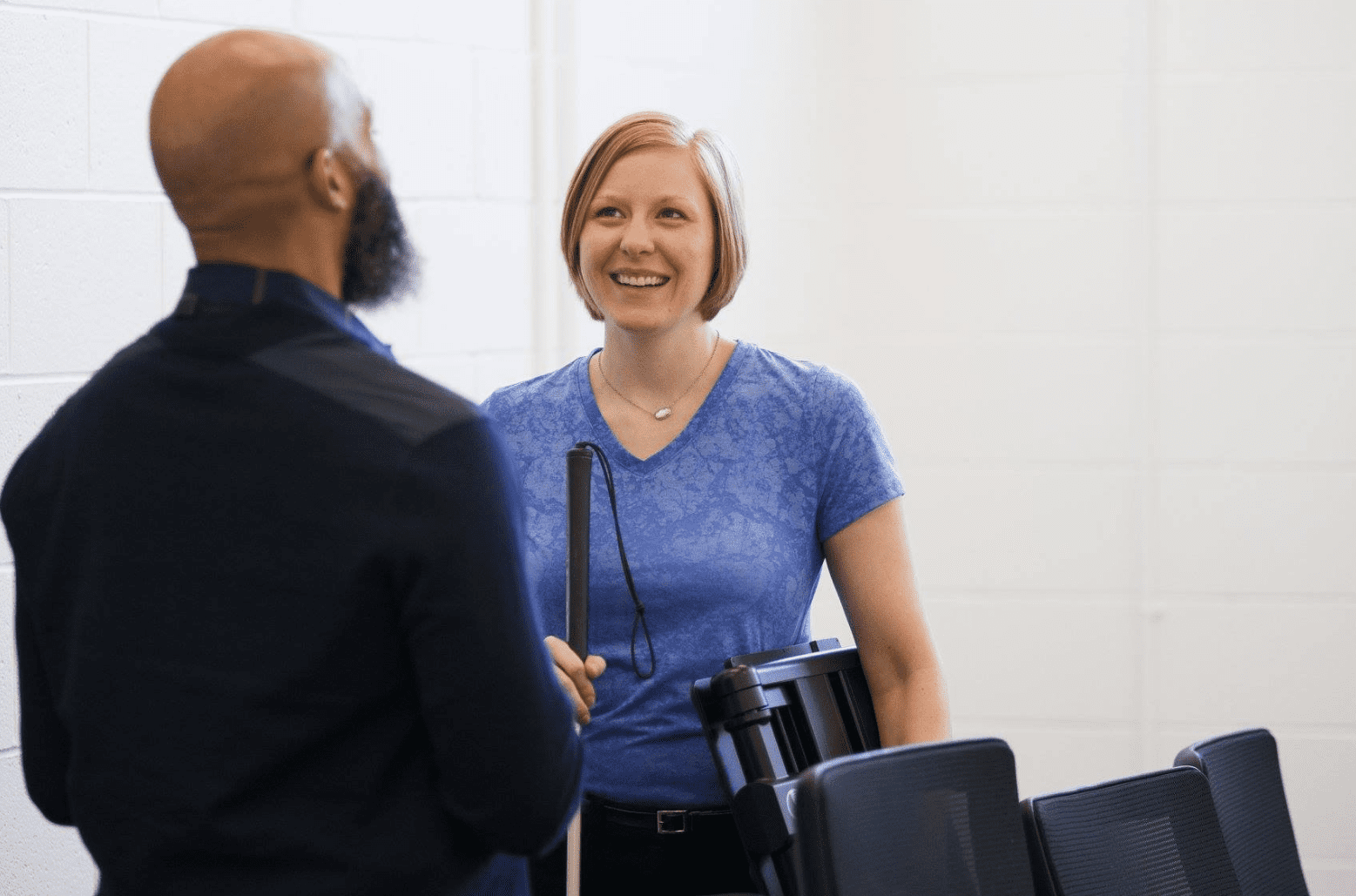 a man and a woman talk in an office setting. the woman is smiling and holding a white cane