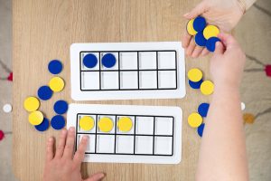 a student uses ten frames and blue and yellow textured discs to do math equations within the plastic frames
