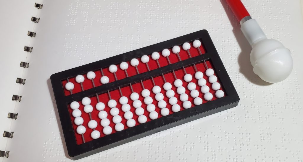 a cranmer's abacus and a white cane laying across the pages of a spiral bound braille book