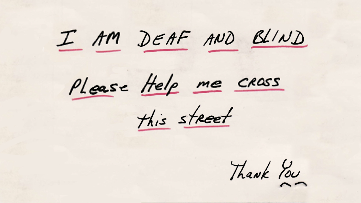 A piece of paper with words in black ink, underlined in red, reading "I AM DEAF AND BLIND. Please Help me cross this street. Thank you."