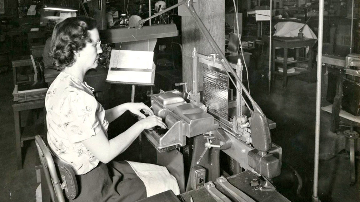 A woman sits in front of a stereograph, a machine for embossing dots onto metal plates. Her fingers rest on six keys, that resemble piano keys. Held snugly in a frame at the back of the machine is a metal plate printing plate.