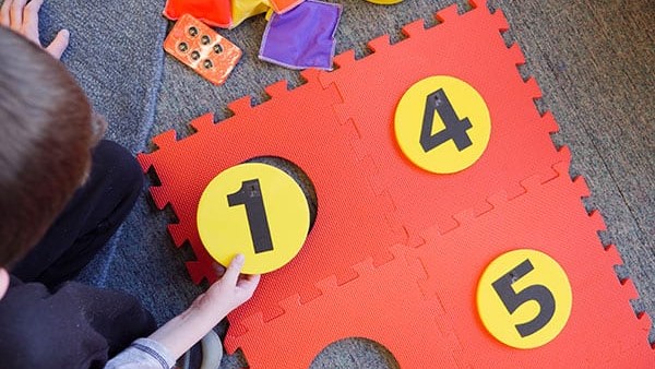 A student placing a foam yellow dot with the number one on it into the red foam floor mat braille cell.