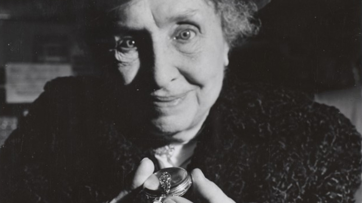 Black and white close up of Helen Keller’s face as she smiles and holds up a pocket watch.